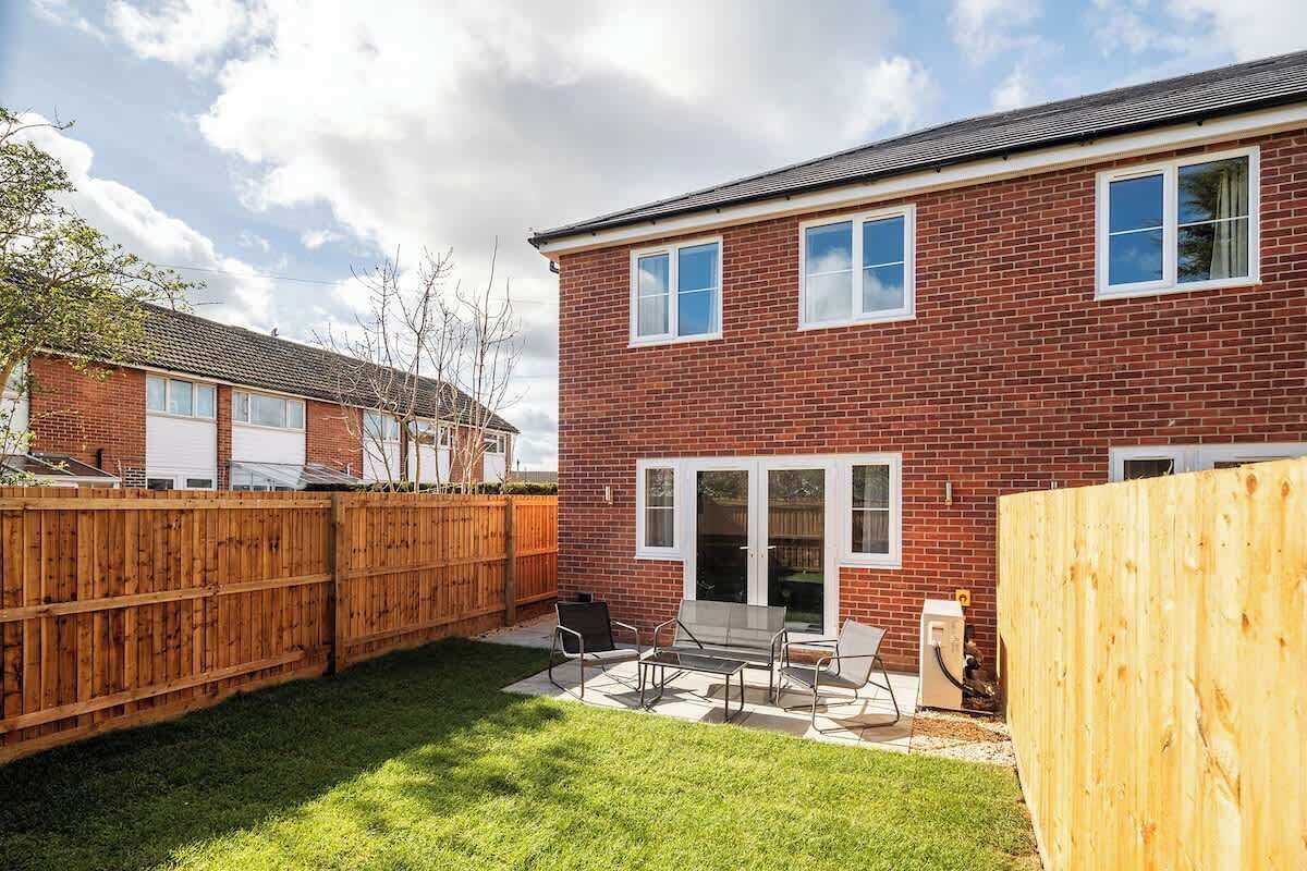 A brick house with a fenced backyard, a patio with outdoor furniture, and a garage.