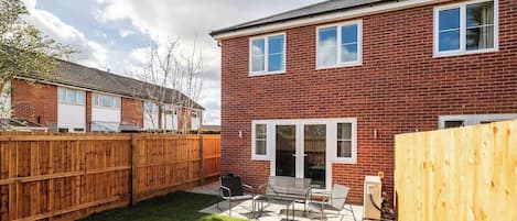 A brick house with a fenced backyard, a patio with outdoor furniture, and a garage.