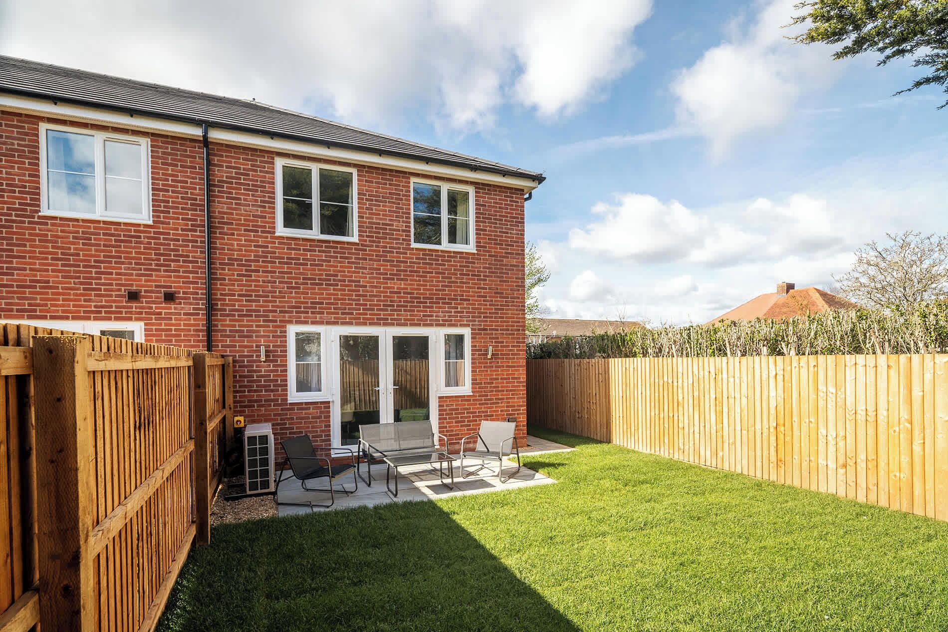 A two-story brick house with a fenced backyard, a patio with outdoor furniture, and a clear sky.