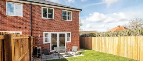 A two-story brick house with a fenced backyard, a patio with outdoor furniture, and a clear sky.