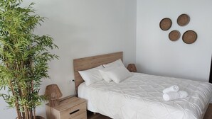 Ein ordentlich eingerichtetes Schlafzimmer mit einem hölzernen Bett, einem Nachttisch mit Schubladen, einem Blumentopf und einer Wandlampe.