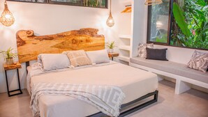 Ein Schlafzimmer mit hohem, rustikalen Holzkopfteil, einem Bett mit vielen Kissen, einer Bank mit Sitzkissen und einem großen Fenster mit Blick auf Grünflächen.