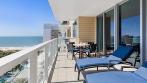 A balcony with a view of the beach, a table with chairs, and a lounge area with blue cushions. - Marriott’s Crystal Shores: 2 Bd. Poolside Family Paradise Awaits on Marco Island (Marco Island)
