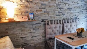 A cozy room with a stone wall, a cushioned bench, a small table with a remote, and a sign that says 'Smile to enter.' - Mini house with full kitchen (Campan)