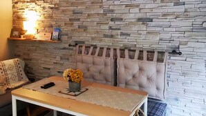 A room with a stone wall, a table with a vase of flowers, a chair, a hanging light fixture, and a radiator. - Mini house with full kitchen (Campan)