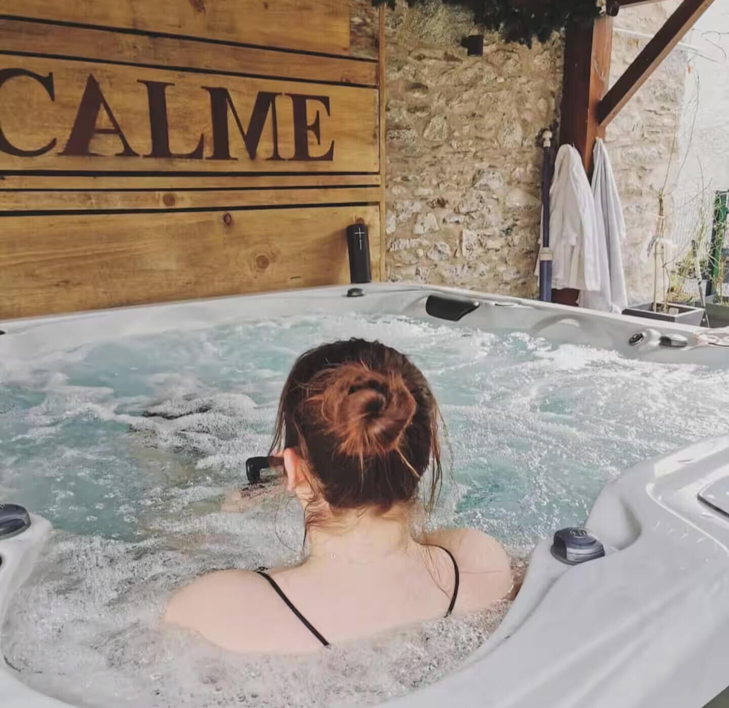 A person in a hot tub with a wooden wall and a sign that reads 'CALME'.