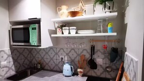 A modern kitchen with a microwave, stove, sink, and decorative items on shelves. - Mini house with full kitchen (Campan)
