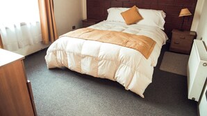 A hotel room with a brick-patterned headboard, a bed with a white comforter and a brown throw, a nightstand with a lamp, and a radiator. - Apartamento en la Patagonia Chilena (Puerto Aysen)