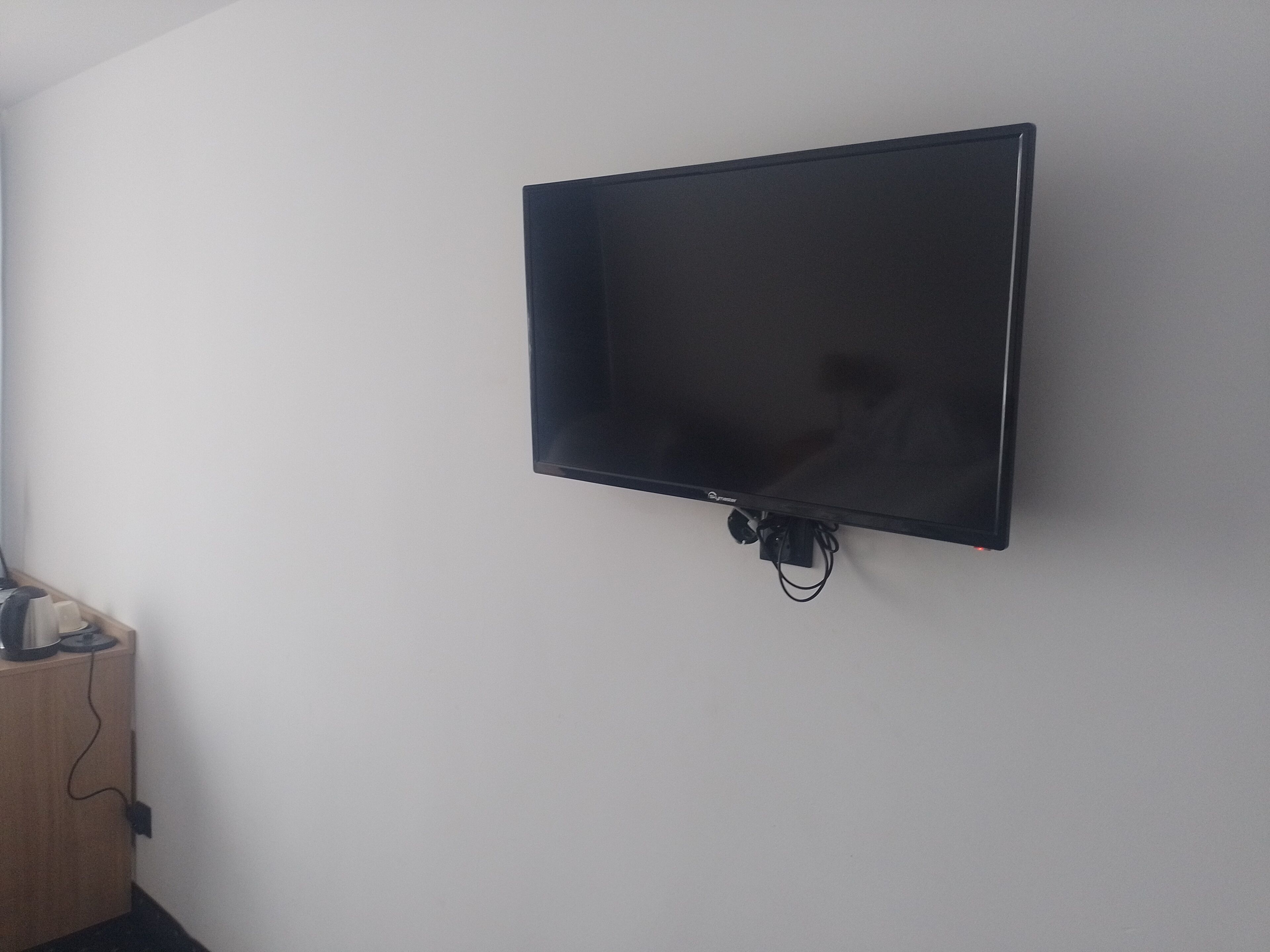 Un televisor de pantalla plana montado en una pared blanca lisa, con un cable de alimentación y un pequeño dispositivo conectado.