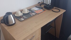 Un escritorio de madera con una tetera, tazas, controles remotos, un teléfono y una lámpara.