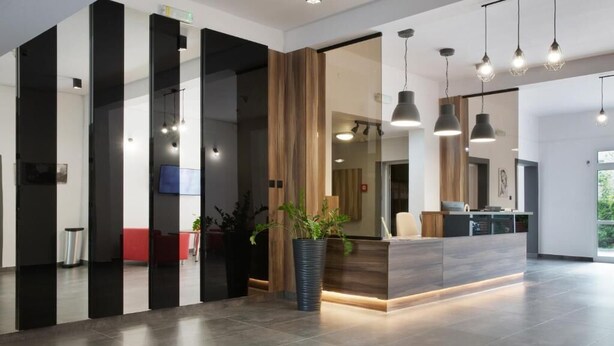 Un área de recepción moderna con mostrador, plantas en macetas e iluminación colgante.