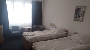 Una habitación de hotel con dos camas individuales, una silla, una mesita y una lámpara.