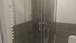 Aseo con cabina de ducha con puerta de cristal, una toalla blanca colgada en la puerta y un inodoro a la derecha.