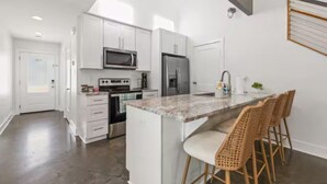 A modern kitchen with white cabinets, stainless steel appliances, a marble island, and wicker bar stools. - Oaks Cottages Modern 2BR Retreat (Lafayette)