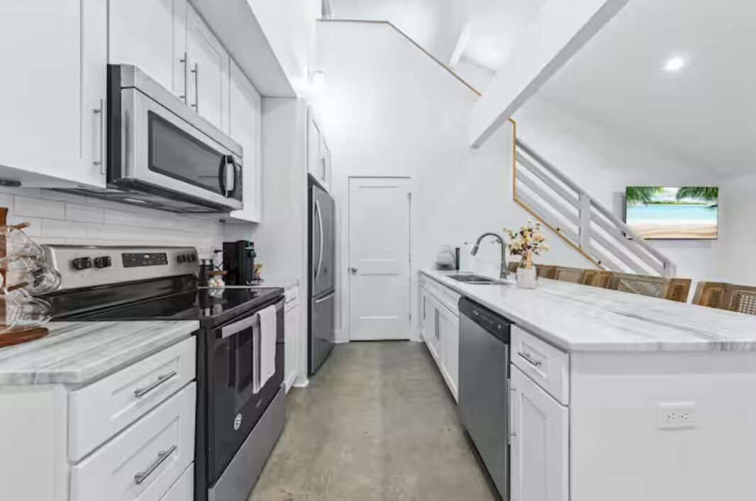 Una cocina moderna con armarios blancos, microondas, estufa y lavavajillas.