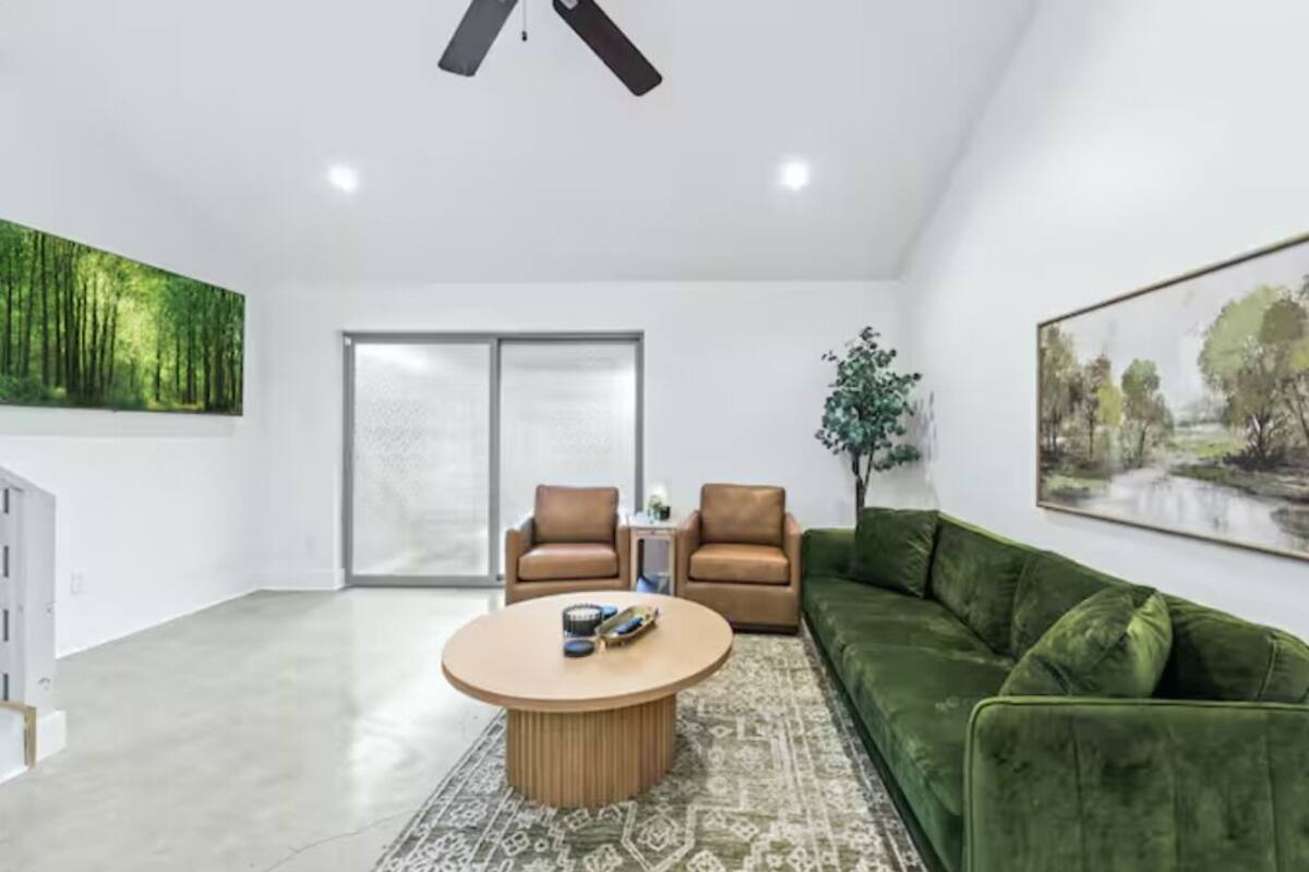 Een moderne woonkamer met een groene bank, twee bruine fauteuils, een ronde salontafel en een plafondventilator.