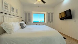 A bedroom with a bed, a window with shutters, a ceiling fan, and a TV mounted on the wall. - Comfy & Updated 4th Floor Condo Princesa E-401 (Puerto Peñasco)