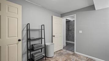 A hallway with a laundry shelf, a trash can, and two doors leading to other rooms.