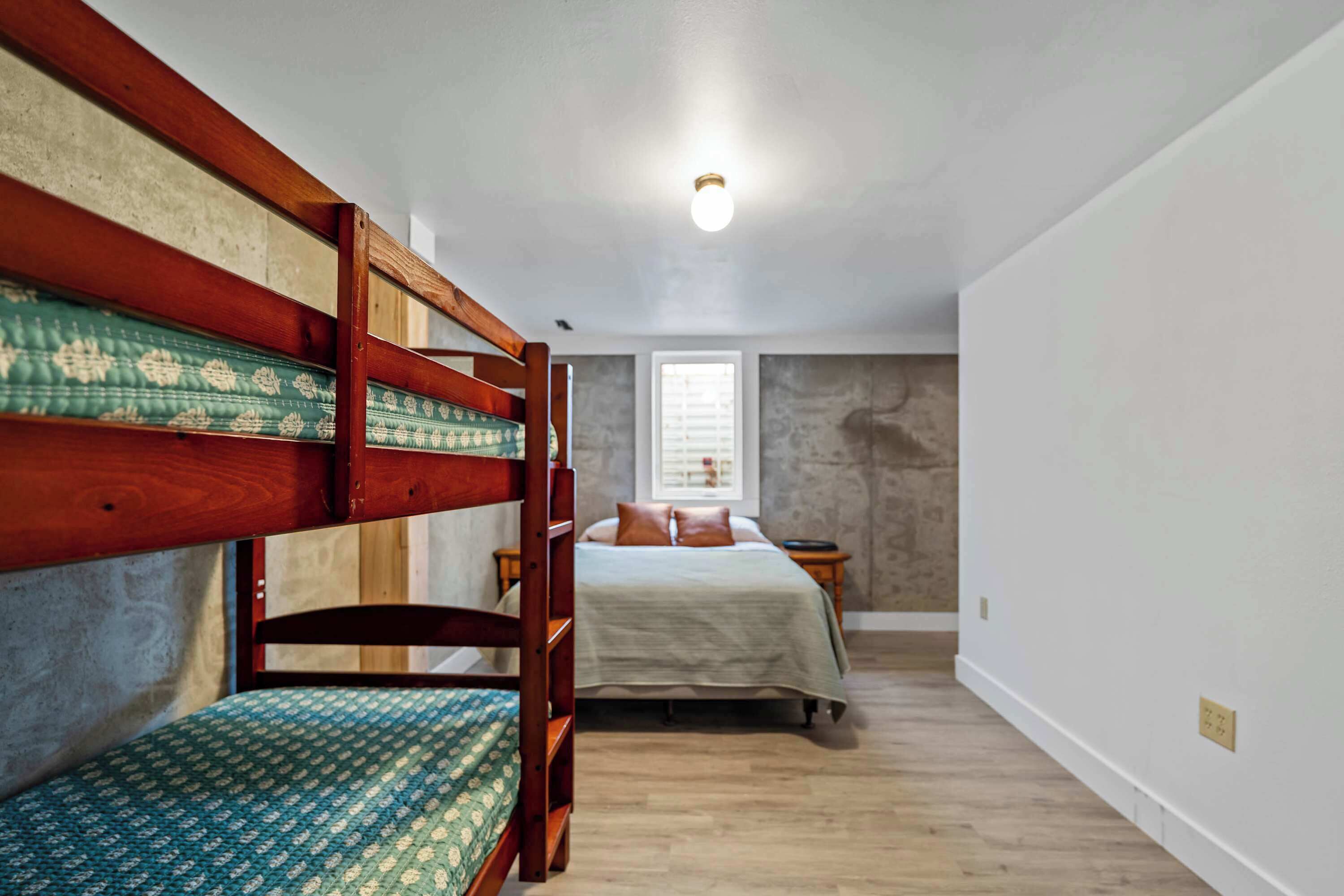 A room with bunk beds, a single bed, a window, and a light fixture.
