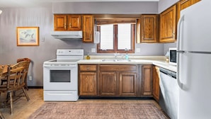 A kitchen with wooden cabinets, a stove, a sink, and a refrigerator. - 3BR-2BA, Sleeps 8 | Close to I-35 (Ames)