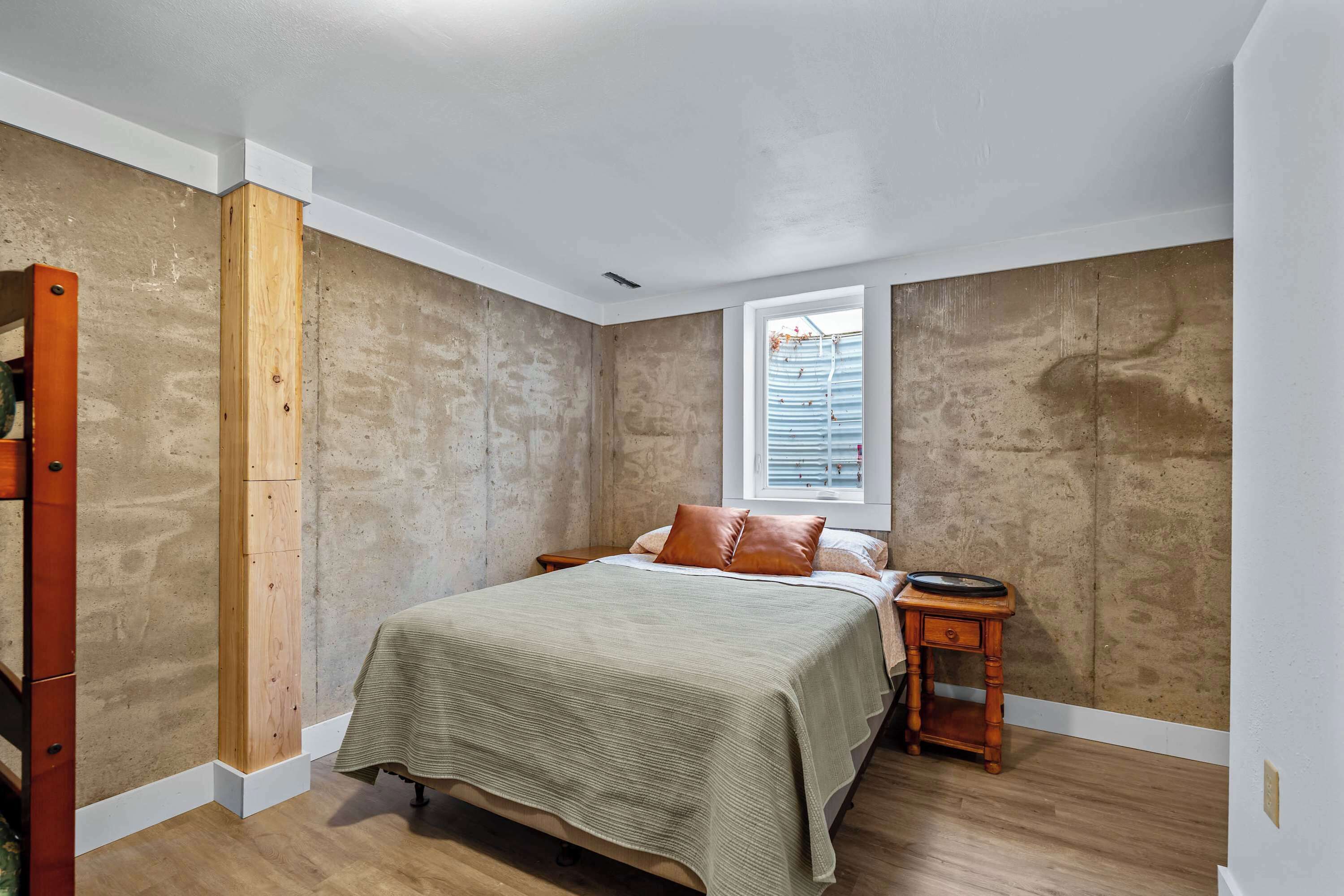 Ein Schlafzimmer mit einem Bett, einem Holzkopfende, einem Fenster und einem kleinen Nachttisch.