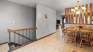 A dining area with a wooden table and chairs, a chandelier, and a staircase with a wooden handrail. - 3BR-2BA, Sleeps 8 | Close to I-35 (Ames)