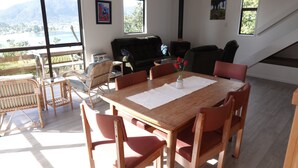 Ein geräumiger Wohnbereich mit einem Holzessttisch, roten Stühlen, einem schwarzen Sofa und großen Fenstern mit Blick ins Freie.