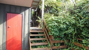 Eine Holztreppe führt zu einer roten Tür, umgeben von dichtem Grün.