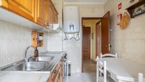 A kitchen with wooden cabinets, a stainless steel sink, a white countertop, a white table, and a white chair. - House Feliz by Centralgarve (Loulé)