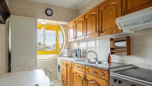A kitchen with wooden cabinets, a stove, a sink, and a window with a yellow frame. - House Feliz by Centralgarve (Loulé)