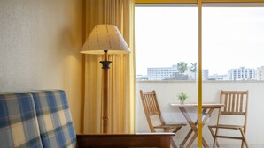 A room with a bed, a sofa, a table with chairs, a lamp, and a view of buildings through a window. - House Feliz by Centralgarve (Loulé)