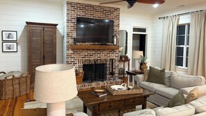 A living room with a brick fireplace, a ceiling fan, a flat-screen TV, a sofa, and a coffee table. - Masters rental -40 mins from tournament (Lincolnton)