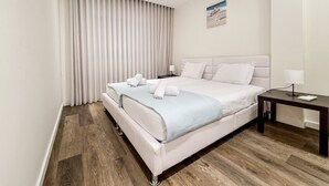 Une chambre d’hôtel avec un grand lit, une table de chevet, une commode, une lampe et une fenêtre avec des rideaux.