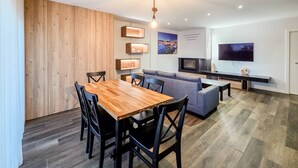 Un salon moderne avec une table à manger en bois, des chaises noires, un canapé gris, un téléviseur et des étagères intégrées.