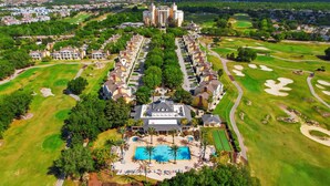 Vista aérea de um resort com piscina central, vários edifícios e campos de golfe.