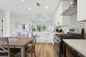 A modern kitchen with white cabinetry, a wooden dining table, and a large stove. - EPIC Seven Eagles Escape (Kissimmee)