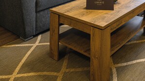 Un salon moderne avec un canapé gris, des coussins jaunes, une table basse en bois sur laquelle se trouve un panier de fruits, et un climatiseur fixé au mur.