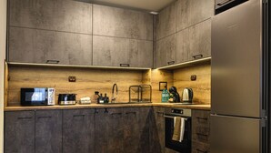 Une cuisine moderne avec des meubles de couleur sombre, un plan de travail en bois et un réfrigérateur en acier inoxydable.