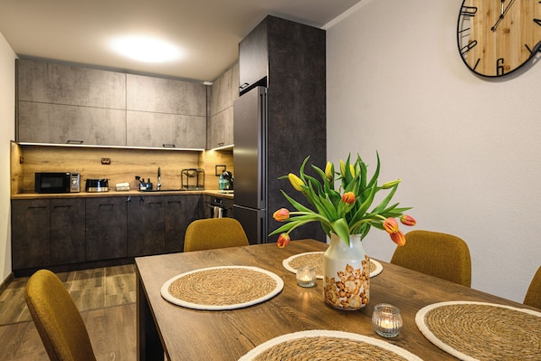 A modern kitchen with dark cabinets, a stainless steel refrigerator, and a wooden dining table with placemats and a vase of tulips.