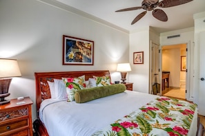 A hotel room with a wooden bed, floral bedspread, two bedside lamps, a ceiling fan, and a framed picture on the wall. - Honua Kai 4 Free Rental Cars KBM Resorts Grand Suite 4 Units, 10 Bedrooms HK Ml-2675 (Kaanapali)
