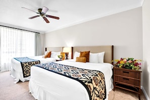 Ein Hotelzimmer mit zwei Betten, einem Deckenventilator, einem Nachttisch mit Lampe und einer Blumenvase.
