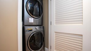 A laundry room with two stacked washing machines and a door with horizontal blinds. - Honua Kai 4 Free Cars KBM Resorts Front Alii Suite 4 Units, 8 Bedrooms HK Ml-3149 (Kaanapali)
