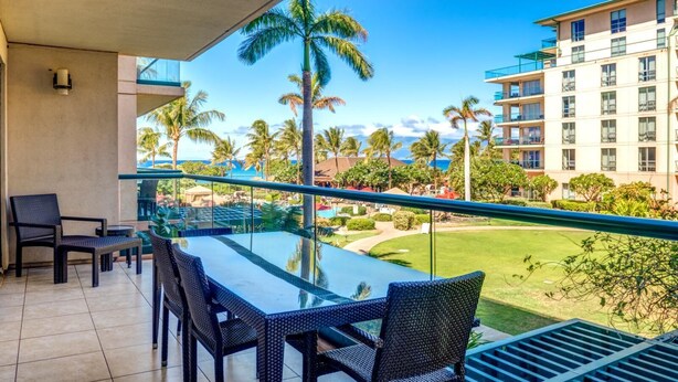 Ein Balkon mit Glastisch und Stühlen, der auf einen Pool und Palmen mit einem Gebäude im Hintergrund blickt.