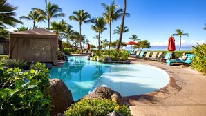 Ein Poolbereich mit Liegestühlen und Sonnenschirmen, umgeben von Palmen und Felsen.