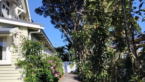 A narrow pathway flanked by lush greenery and a white building with a gabled roof. - LLU HOMES FOR EXPLORERS (Westport)