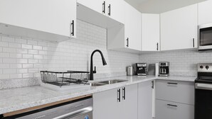 Una cocina moderna con armarios blancos, lavavajillas de acero inoxidable, grifo negro y microondas.