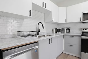 A modern kitchen with white cabinets, a stainless steel dishwasher, a black faucet, and a microwave.