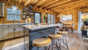 A wooden cabin interior with a kitchen, dining area, and bar. - Timber Breeze - game room, hot tub, pets, firepit (Blue Ridge)