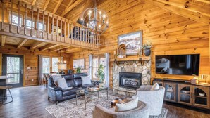 A spacious log cabin interior with a fireplace, a large TV, and a cozy seating area. - Timber Breeze - game room, hot tub, pets, firepit (Blue Ridge)