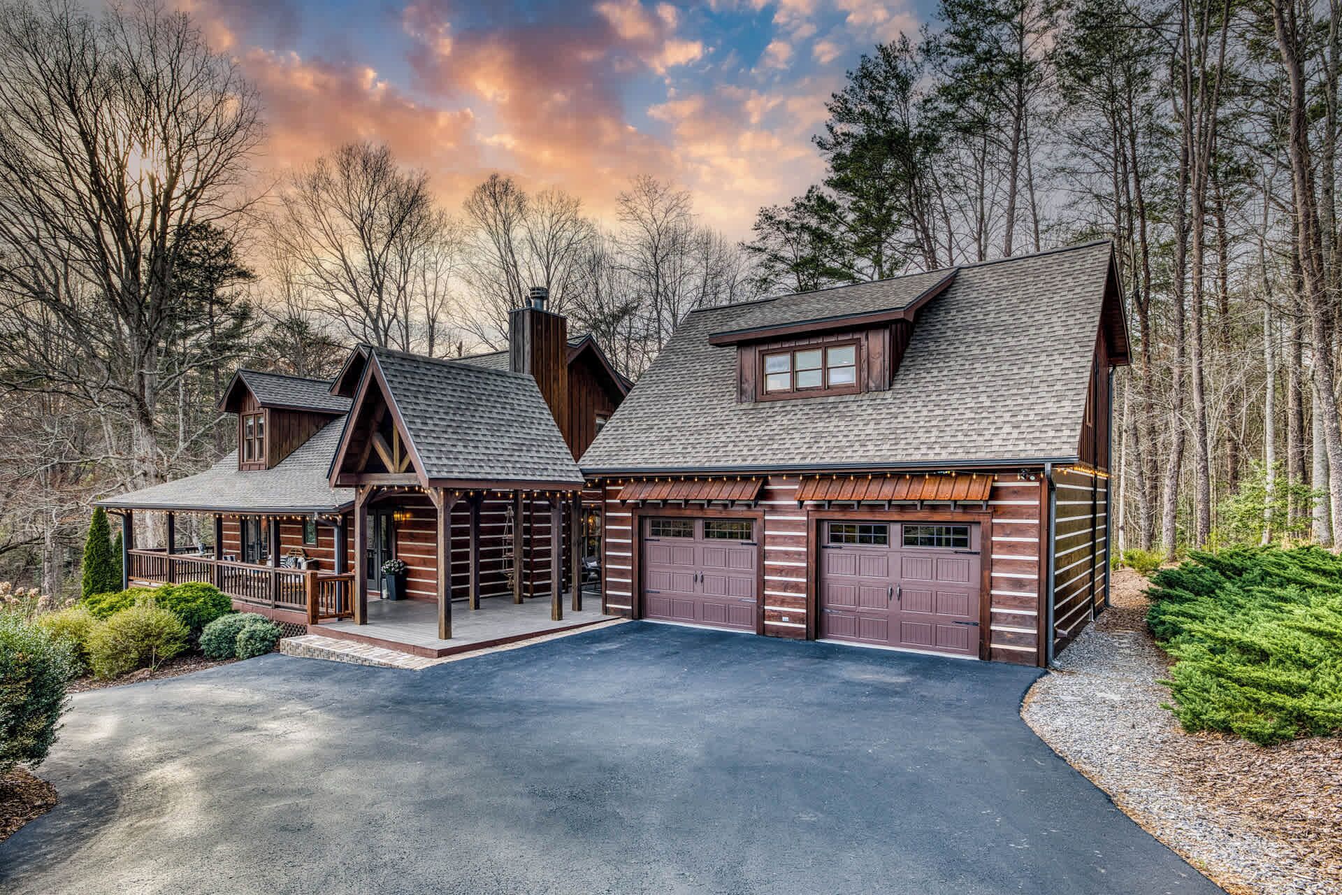 A log cabin with a covered porch, a garage, and a driveway.